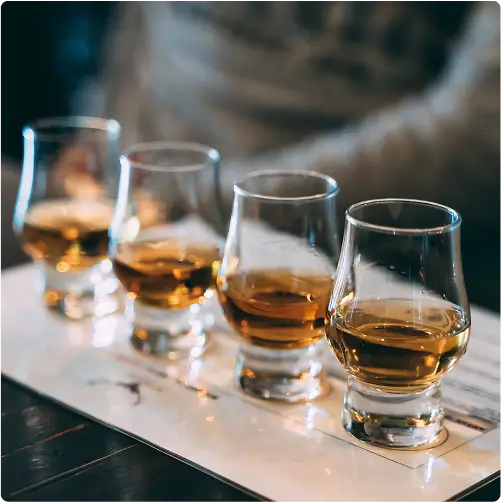 Four glasses of whiskey are lined up on a table