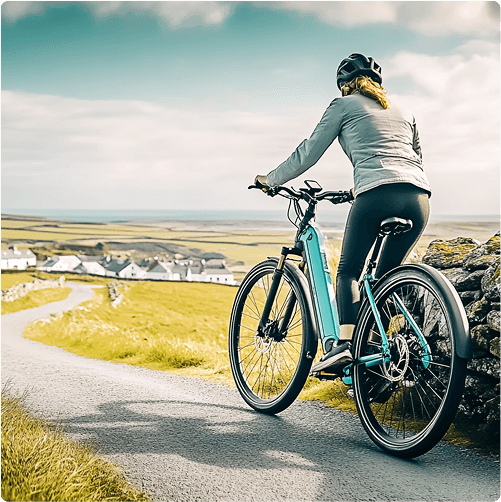 A person wearing a helmet and jacket rides an e-Whizz Electric bike on a winding country road, overlooking a village and fields under a partly cloudy sky.